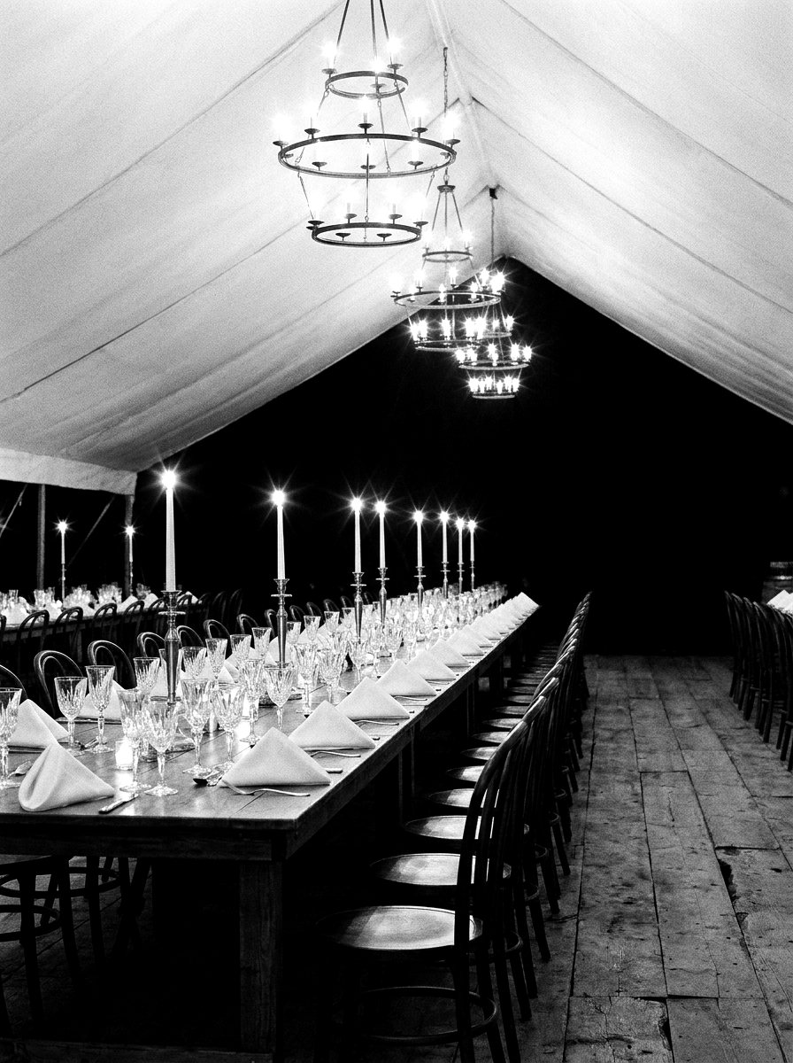 A candlelit banquet table beneath chandeliers inside a marquee